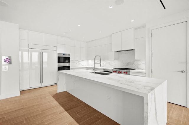 kitchen featuring stainless steel appliances, white cabinetry, sink, an island with sink, and light hardwood / wood-style flooring