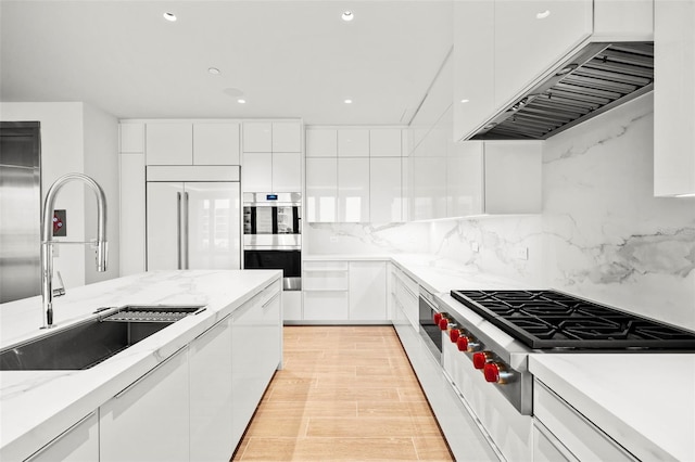 kitchen with stainless steel appliances, white cabinetry, sink, light wood-type flooring, and decorative backsplash