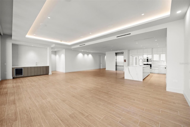 unfurnished living room with light hardwood / wood-style floors, sink, and a raised ceiling