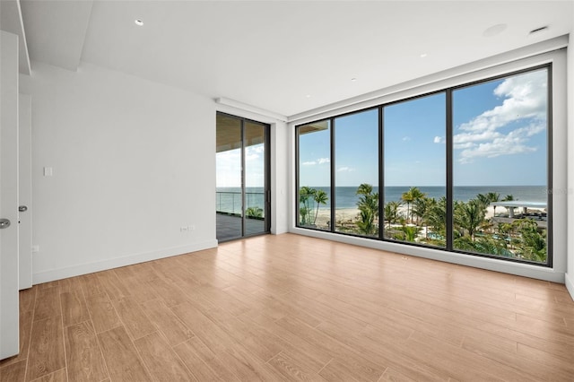 unfurnished room featuring light wood-type flooring, a water view, and a wall of windows