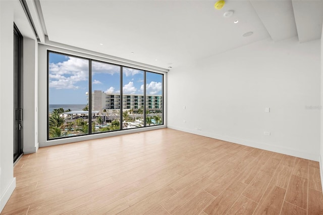 empty room featuring a water view, floor to ceiling windows, and light hardwood / wood-style floors