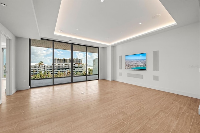 unfurnished living room featuring a raised ceiling, light hardwood / wood-style flooring, and floor to ceiling windows