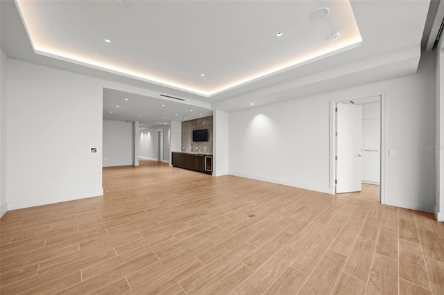 unfurnished living room with light wood-type flooring and a tray ceiling