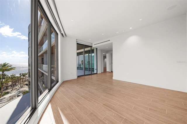 empty room with expansive windows, light wood-type flooring, and a water view