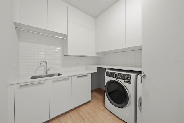 clothes washing area featuring washer / clothes dryer, cabinets, sink, and light hardwood / wood-style flooring