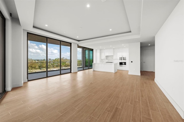 unfurnished living room with light hardwood / wood-style flooring and a tray ceiling