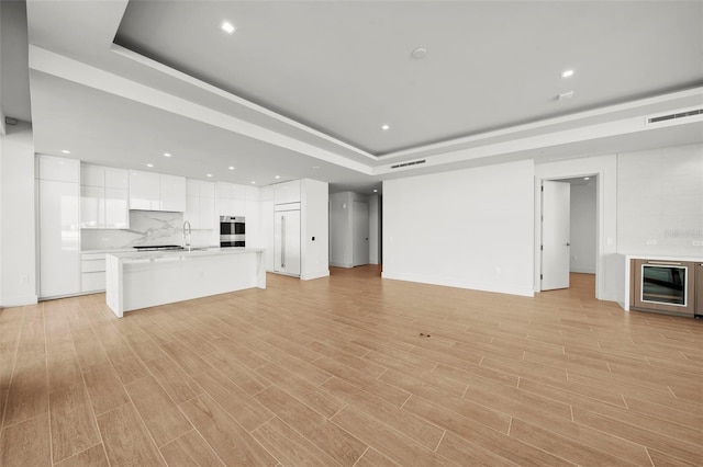 unfurnished living room featuring light hardwood / wood-style floors, sink, and a raised ceiling