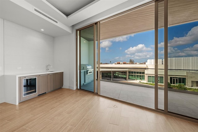 interior space featuring light wood-type flooring, a wall of windows, sink, and wine cooler