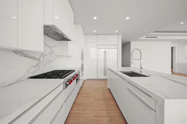 kitchen with paneled built in refrigerator, white cabinetry, sink, and light wood-type flooring