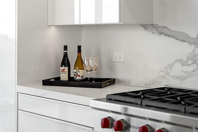 interior details with white cabinetry, stainless steel range, indoor bar, and backsplash