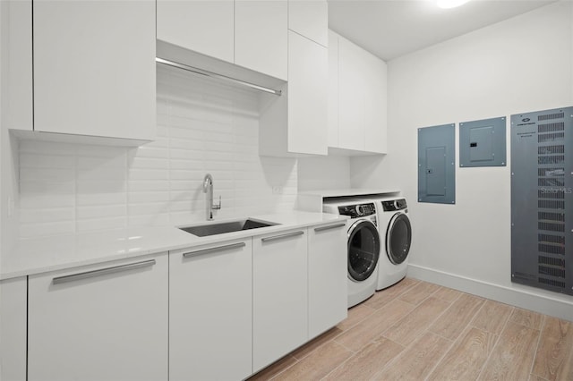 clothes washing area with electric panel, cabinets, sink, light hardwood / wood-style flooring, and washer and dryer