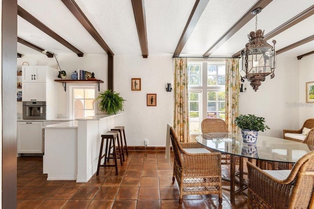 dining space with beamed ceiling, dark tile patterned floors, and an inviting chandelier