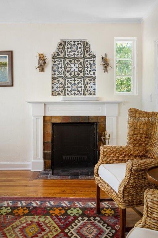 living area with crown molding, wood-type flooring, and a tiled fireplace