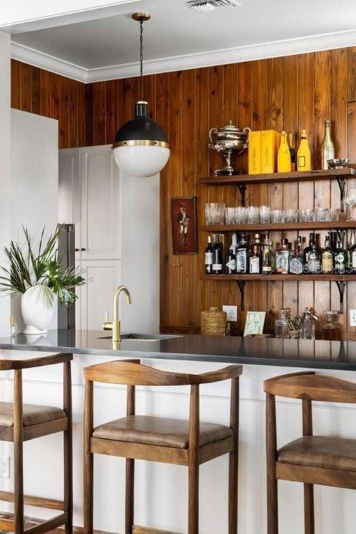 bar featuring ornamental molding, sink, wooden walls, and decorative light fixtures