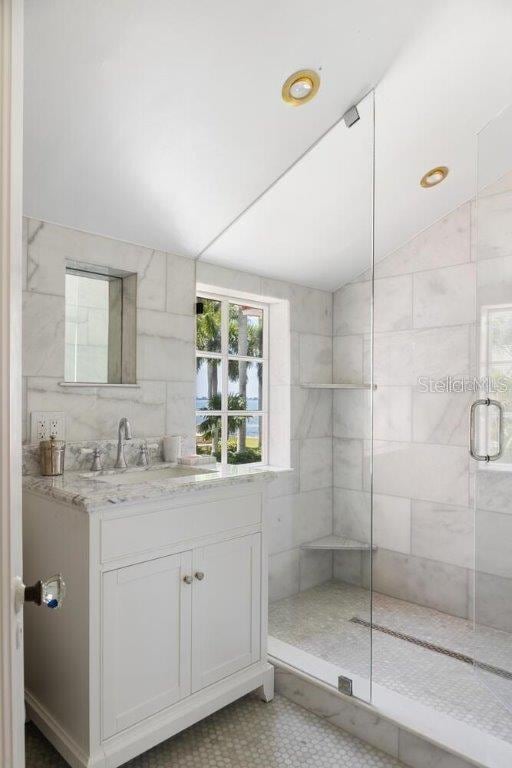 bathroom with vanity, vaulted ceiling, a shower with door, and tile walls