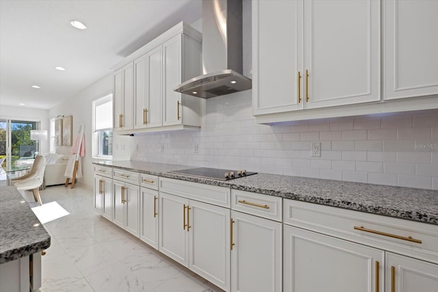 kitchen featuring black electric stovetop, wall chimney exhaust hood, decorative backsplash, light stone counters, and white cabinetry