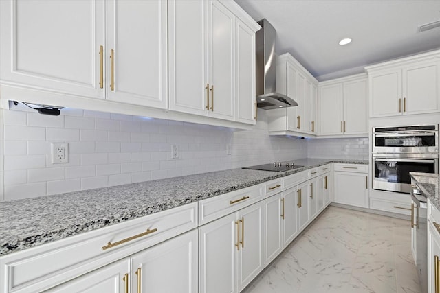 kitchen featuring black electric stovetop, wall chimney range hood, white cabinetry, light stone counters, and stainless steel double oven