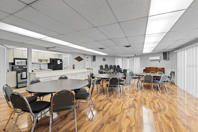 dining room with light wood-type flooring, a wall unit AC, and a paneled ceiling