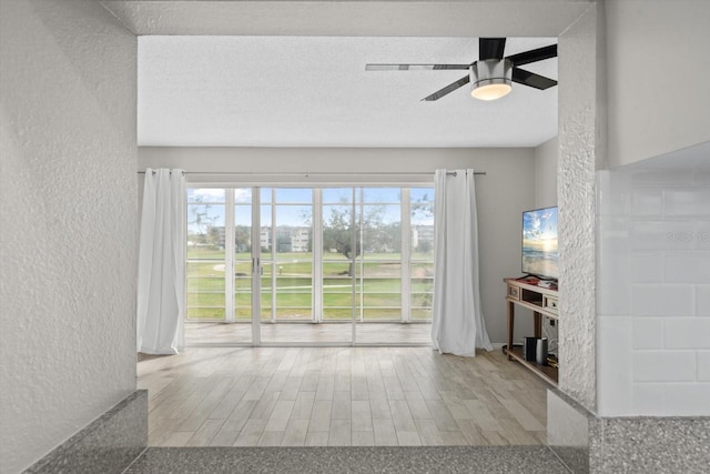 unfurnished living room featuring ceiling fan, light hardwood / wood-style floors, and a textured ceiling