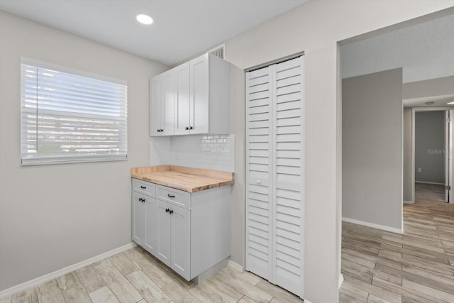 kitchen with wooden counters, light wood-type flooring, and white cabinetry