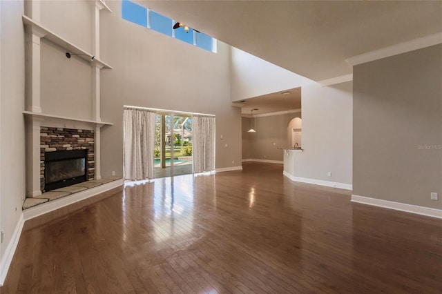 unfurnished living room featuring hardwood / wood-style flooring, a stone fireplace, ornamental molding, and a high ceiling