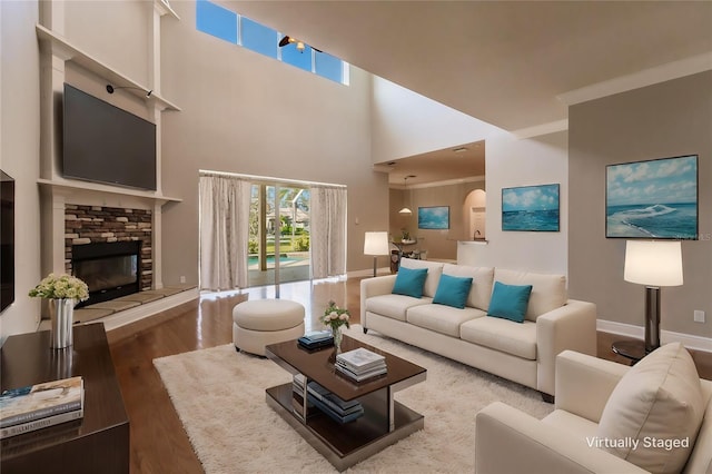 living room with hardwood / wood-style floors, a stone fireplace, crown molding, and a high ceiling