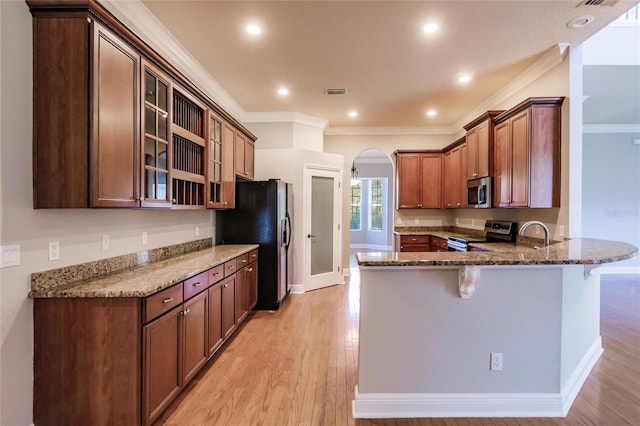 kitchen featuring stainless steel appliances, light hardwood / wood-style flooring, kitchen peninsula, a kitchen bar, and ornamental molding