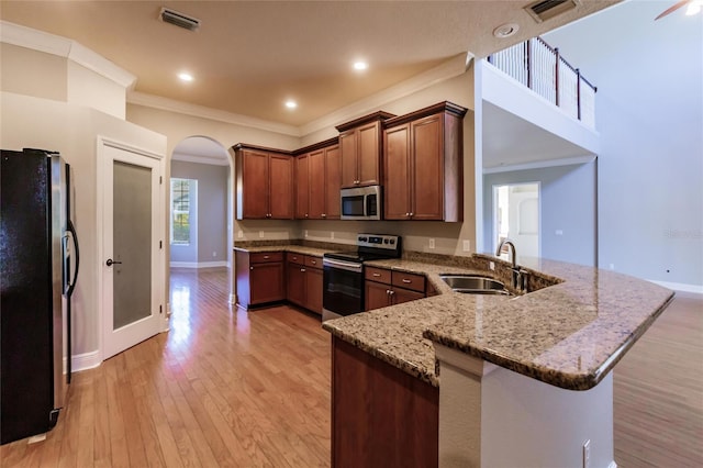 kitchen featuring sink, light wood-type flooring, appliances with stainless steel finishes, light stone counters, and kitchen peninsula