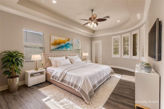 bedroom with a raised ceiling, ceiling fan, and dark wood-type flooring