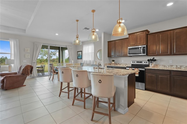 kitchen with a center island with sink, appliances with stainless steel finishes, decorative light fixtures, light tile patterned flooring, and a kitchen bar