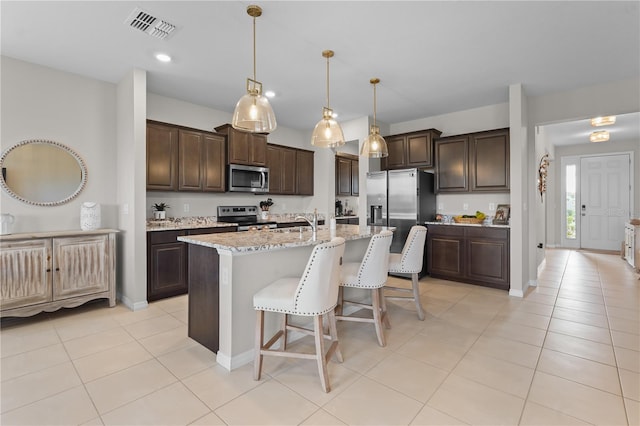 kitchen featuring hanging light fixtures, a center island with sink, stainless steel appliances, and dark brown cabinets