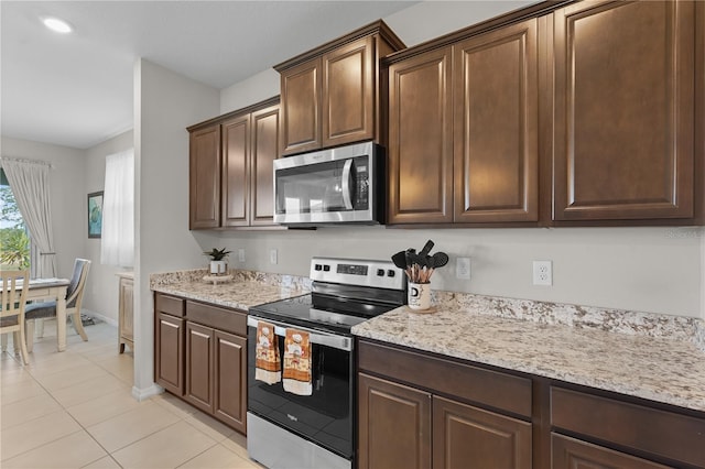 kitchen featuring appliances with stainless steel finishes, light stone counters, dark brown cabinets, and light tile patterned flooring