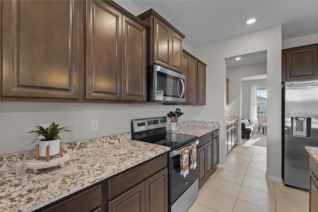 kitchen with light tile patterned floors, dark brown cabinetry, stainless steel appliances, and light stone counters