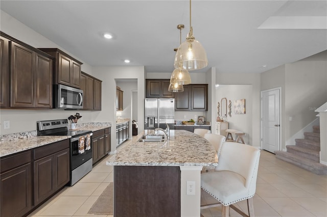 kitchen featuring pendant lighting, a center island with sink, light tile patterned floors, dark brown cabinetry, and stainless steel appliances