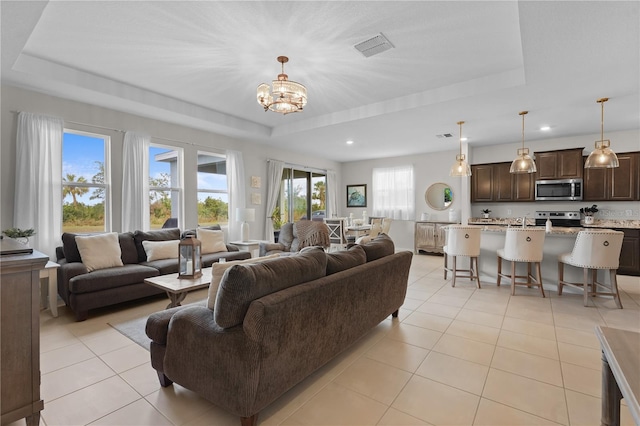 living room featuring a raised ceiling, light tile patterned flooring, and an inviting chandelier