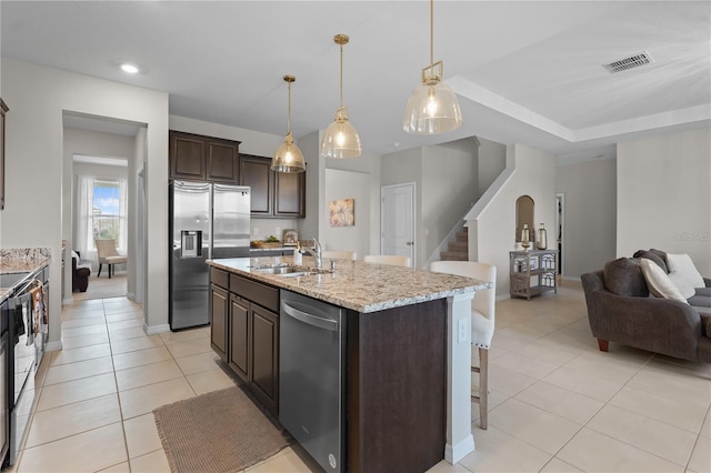 kitchen with a kitchen island with sink, dark brown cabinetry, stainless steel appliances, a sink, and open floor plan