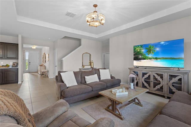 living area featuring light tile patterned floors, visible vents, a tray ceiling, and a chandelier