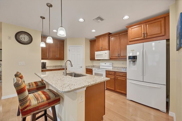 kitchen with sink, a center island with sink, white appliances, and light wood-type flooring