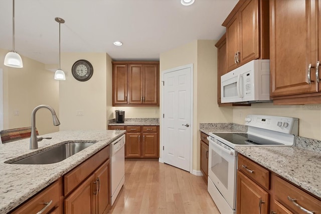 kitchen with sink, hanging light fixtures, white appliances, light hardwood / wood-style floors, and light stone counters