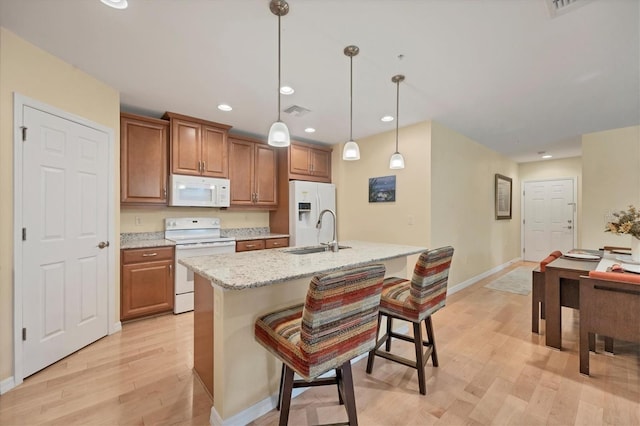 kitchen featuring white appliances, sink, decorative light fixtures, a center island with sink, and light hardwood / wood-style flooring