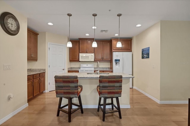 kitchen with sink, light stone counters, an island with sink, white appliances, and light wood-type flooring