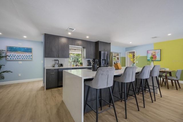 kitchen with a breakfast bar area, stainless steel refrigerator with ice dispenser, dark brown cabinets, a center island, and light hardwood / wood-style floors