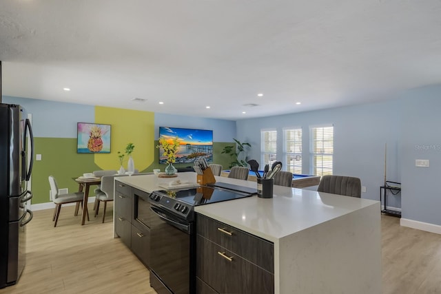 kitchen with a kitchen island, stainless steel fridge, dark brown cabinetry, black / electric stove, and light hardwood / wood-style flooring