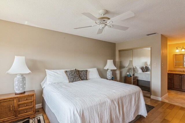 bedroom with connected bathroom, ceiling fan, light hardwood / wood-style flooring, a textured ceiling, and a closet