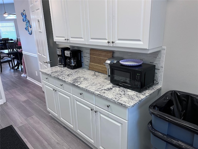 kitchen featuring white cabinetry, light wood-type flooring, light stone counters, and tasteful backsplash