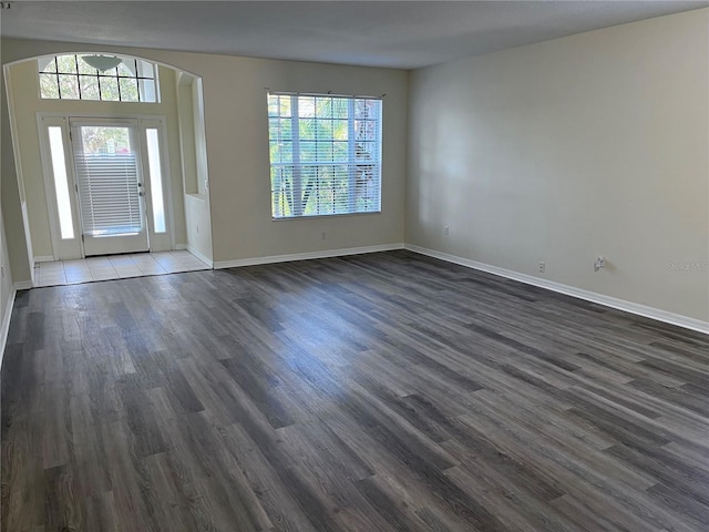 entrance foyer featuring a wealth of natural light, dark wood finished floors, arched walkways, and baseboards