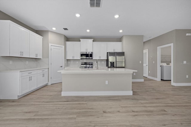 kitchen featuring washer and clothes dryer, backsplash, a center island with sink, and stainless steel appliances