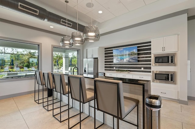 kitchen featuring white cabinets, stainless steel appliances, hanging light fixtures, and a breakfast bar area