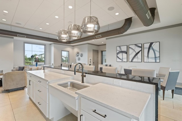 kitchen with decorative light fixtures, white cabinetry, sink, and a center island with sink