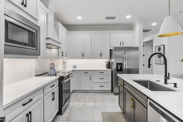 kitchen with stainless steel appliances, decorative light fixtures, custom range hood, sink, and white cabinets